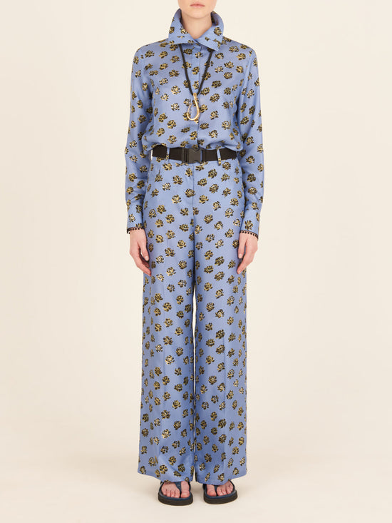 A person is depicted from the back wearing the Emine Pant in periwinkle, a blue floral-patterned outfit with a high collar and long sleeves, featuring wide-legged printed trousers.