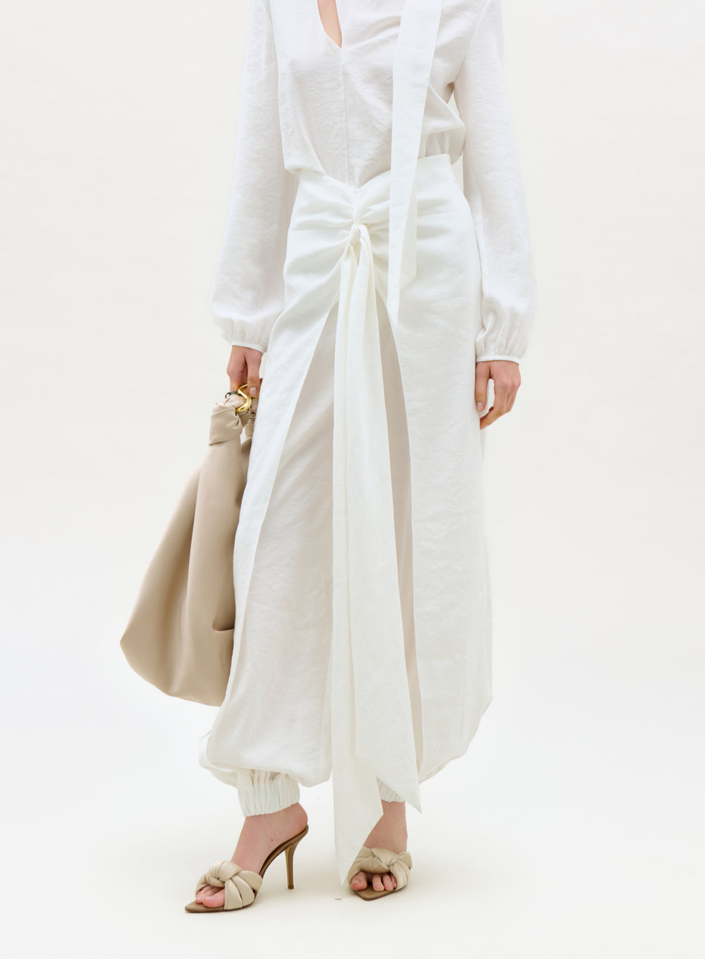 Person wearing a white outfit with wide-leg pants and holding a beige handbag on a white background