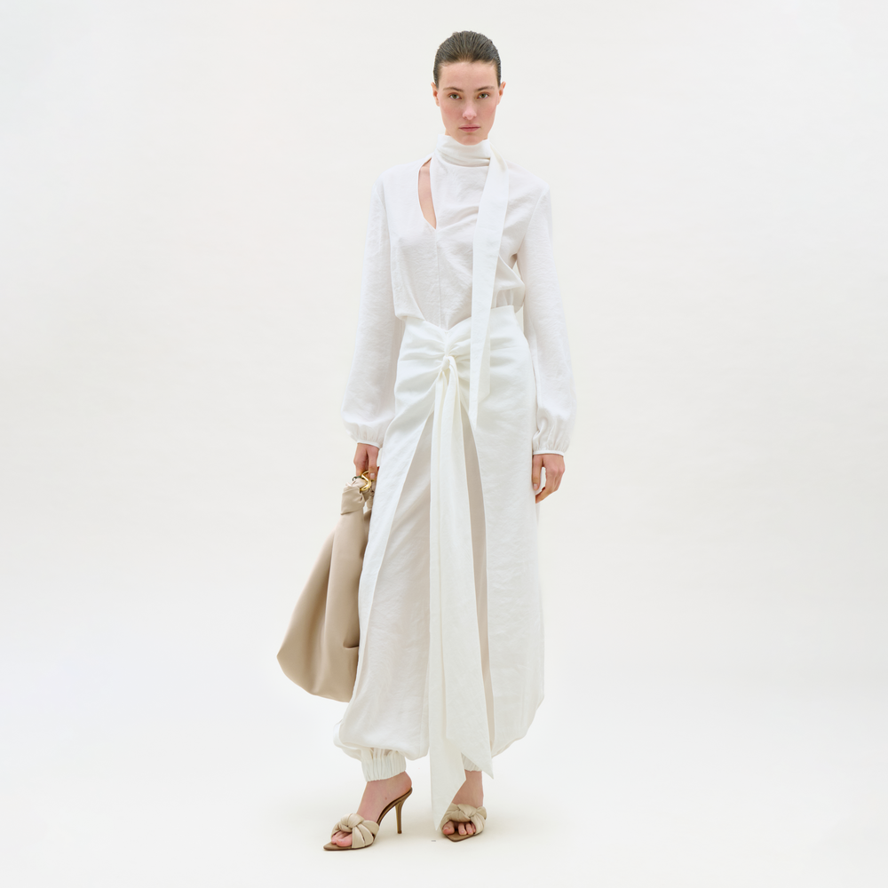 Woman wearing a white outfit with a beige handbag on a white background