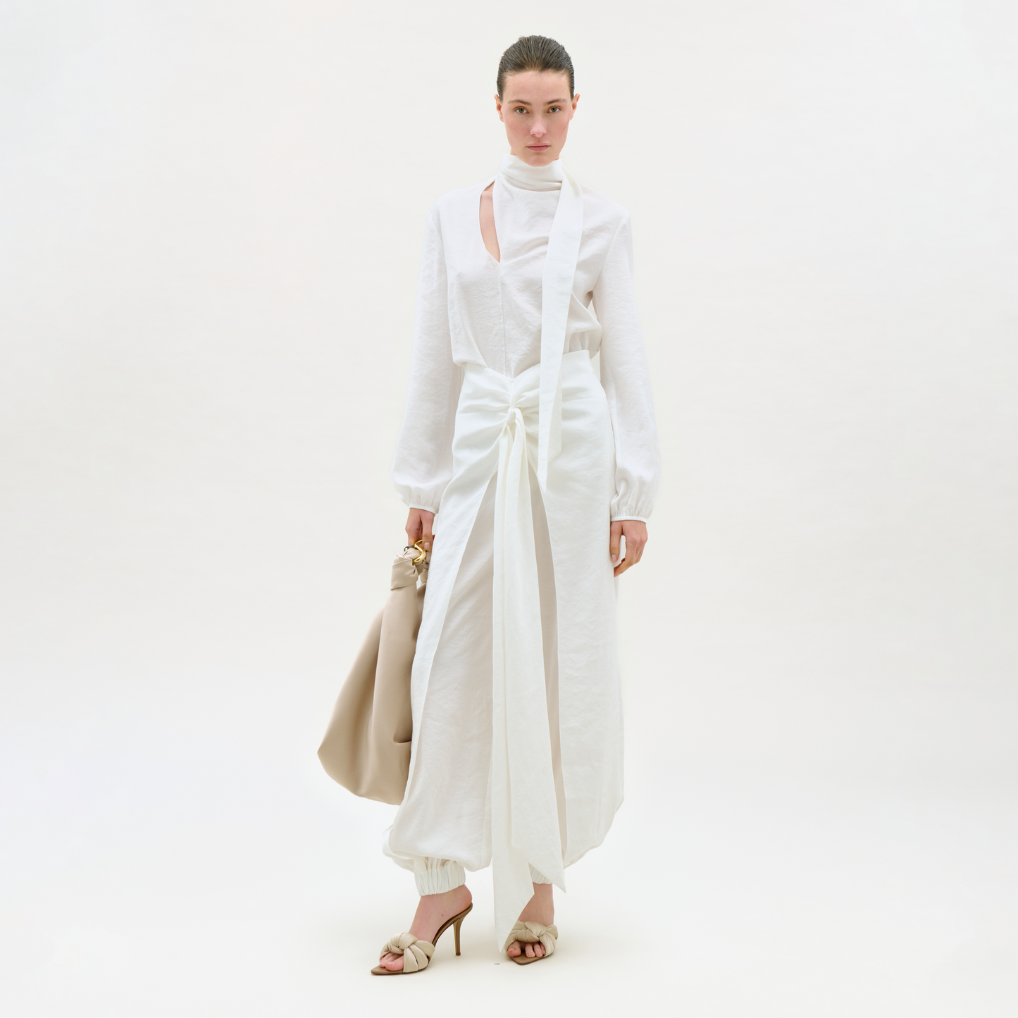 Woman wearing a white outfit with a beige handbag on a white background