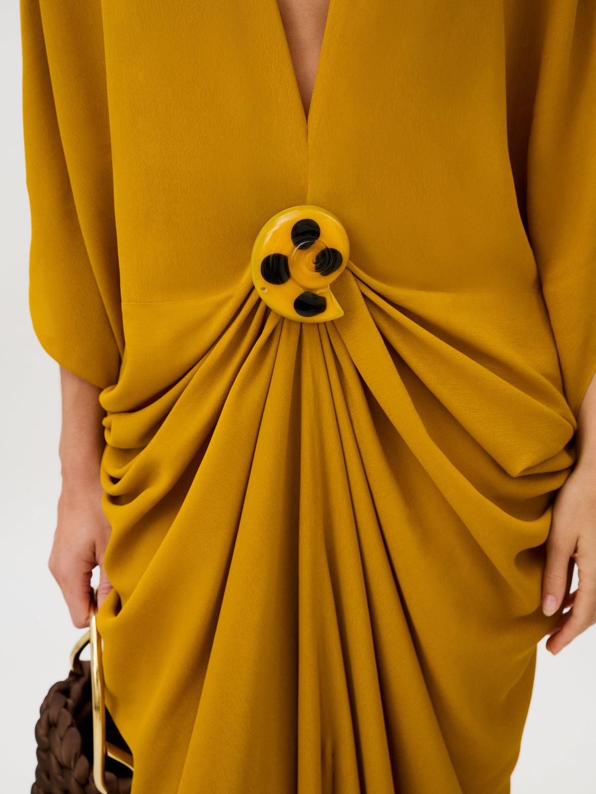 Fiore Tunic in mustard yellow Italian fabric, featuring a deep V-neck and a large, circular yellow and black abstract brooch that gathers the fabric at the waist.