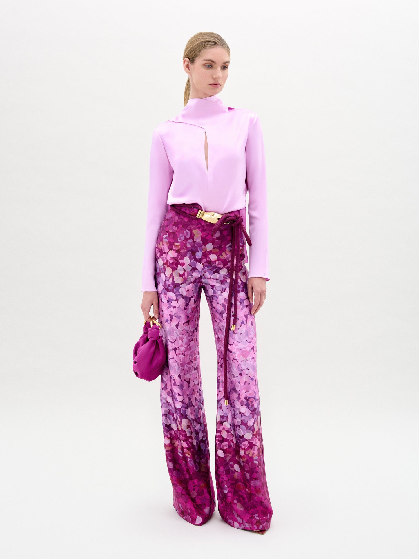 A person wearing a pink top and the Como Pant in purple, crafted from Italian fabric, holds a pink bag against a plain background.