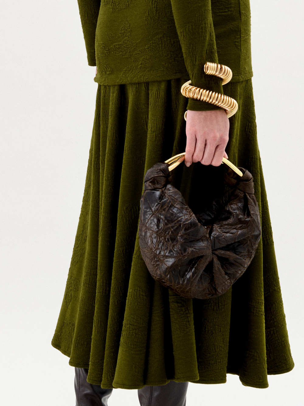 Person wearing a green dress holding a brown leather handbag against a white background