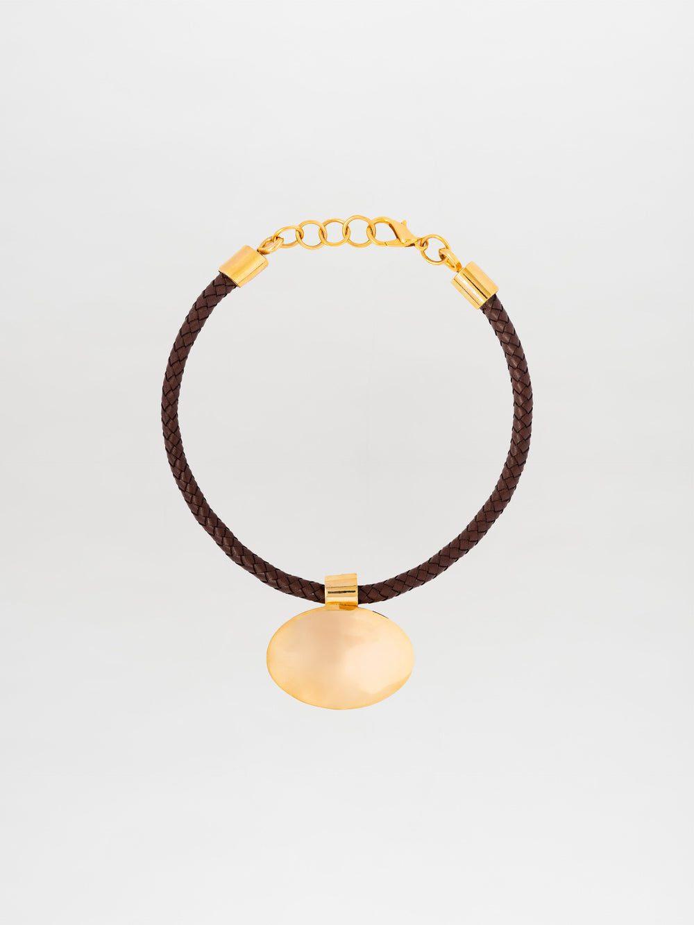 The Gimena Necklace, crafted in Colombia, is a braided brown leather bracelet adorned with gold embellishments such as a chain clasp and a round gold pendant.