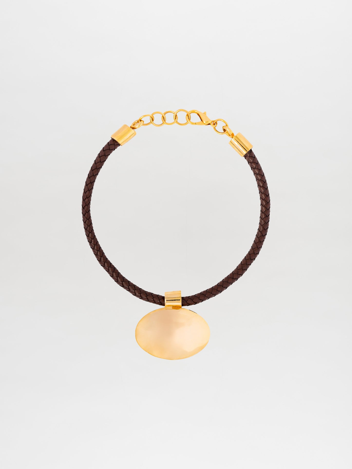 The Gimena Necklace, crafted in Colombia, is a braided brown leather bracelet adorned with gold embellishments such as a chain clasp and a round gold pendant.