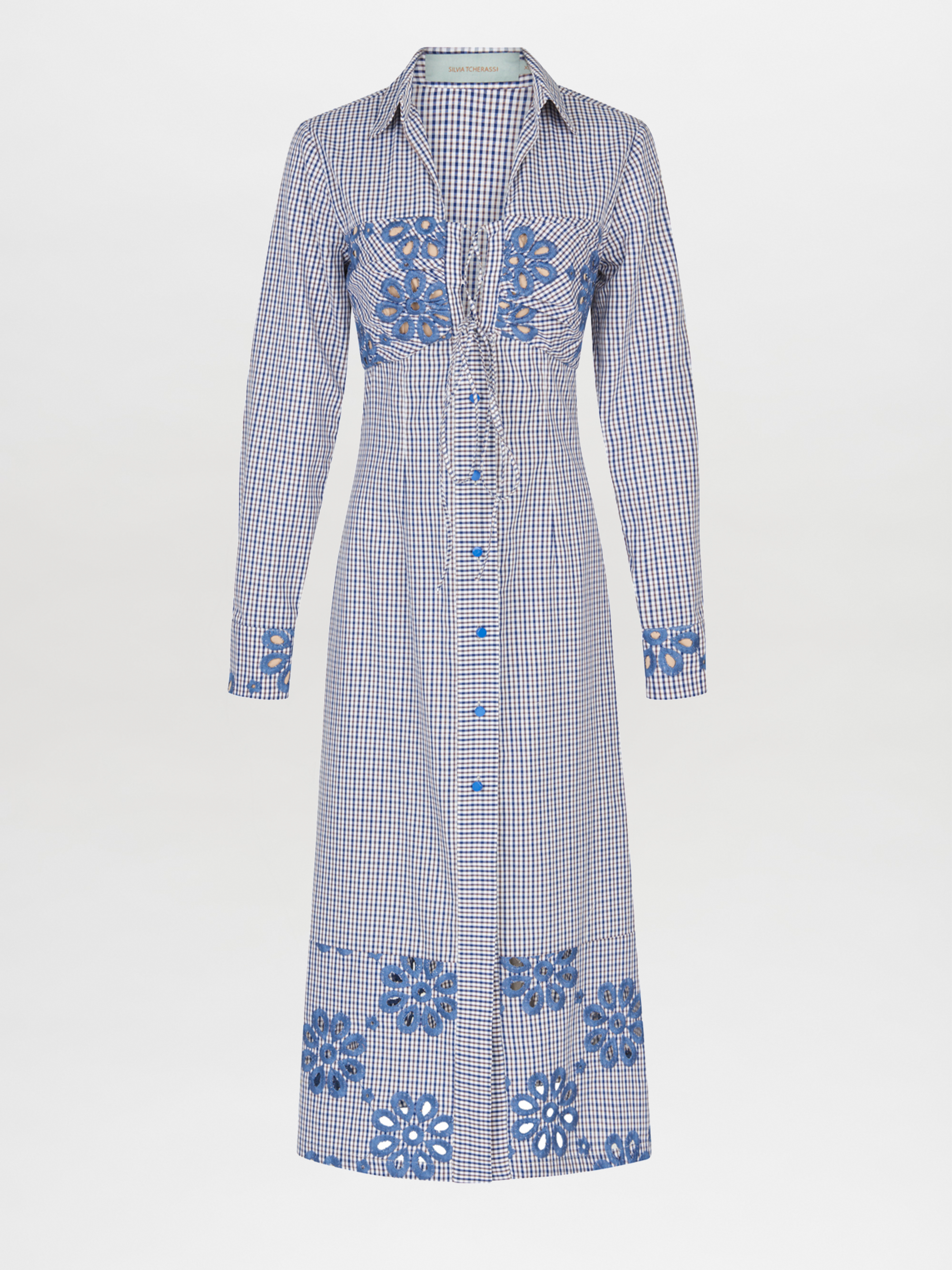 The Ganzoni Dress Navy Floral is a long-sleeve, button-down dress with a collar, featuring a blue and white checkered pattern and blue floral designs. This item is part of our Final Sale and is not eligible for return or exchange.