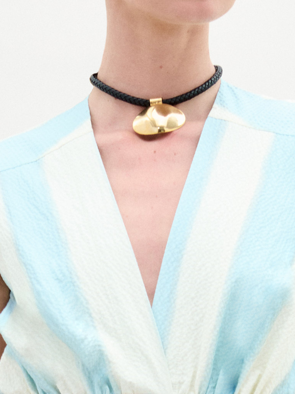 The Gimena Necklace features a gold disc pendant on a dark brown braided cord with gold accents and an adjustable chain clasp. Made in Colombia.
