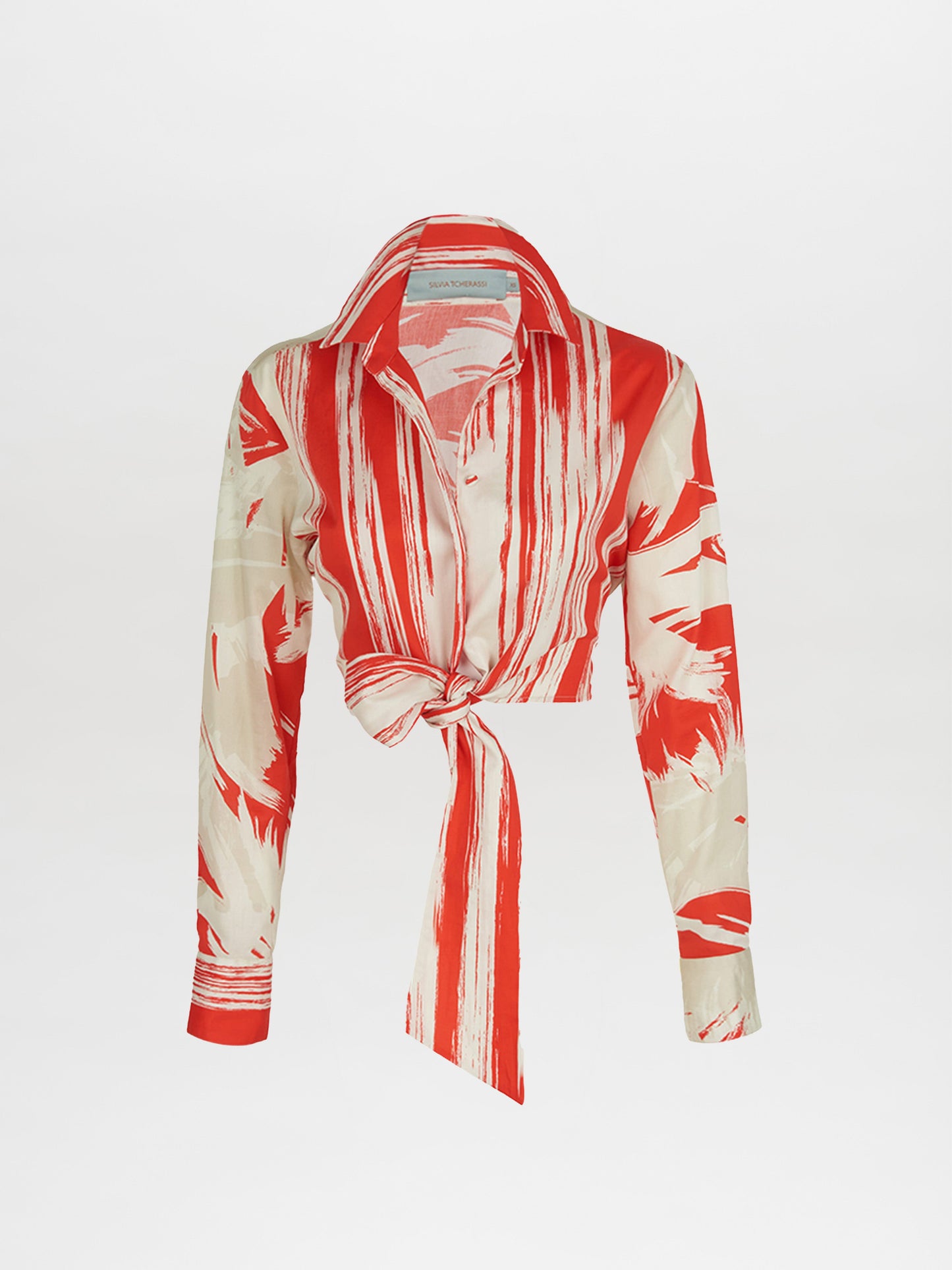 The Gisela Blouse Coral Red Palm Print by Silvia Tcherassi showcases a long-sleeve, button-up design with coral red palm print fabric, featuring abstract stripes and a stylish collar with a tied knot at the waist.