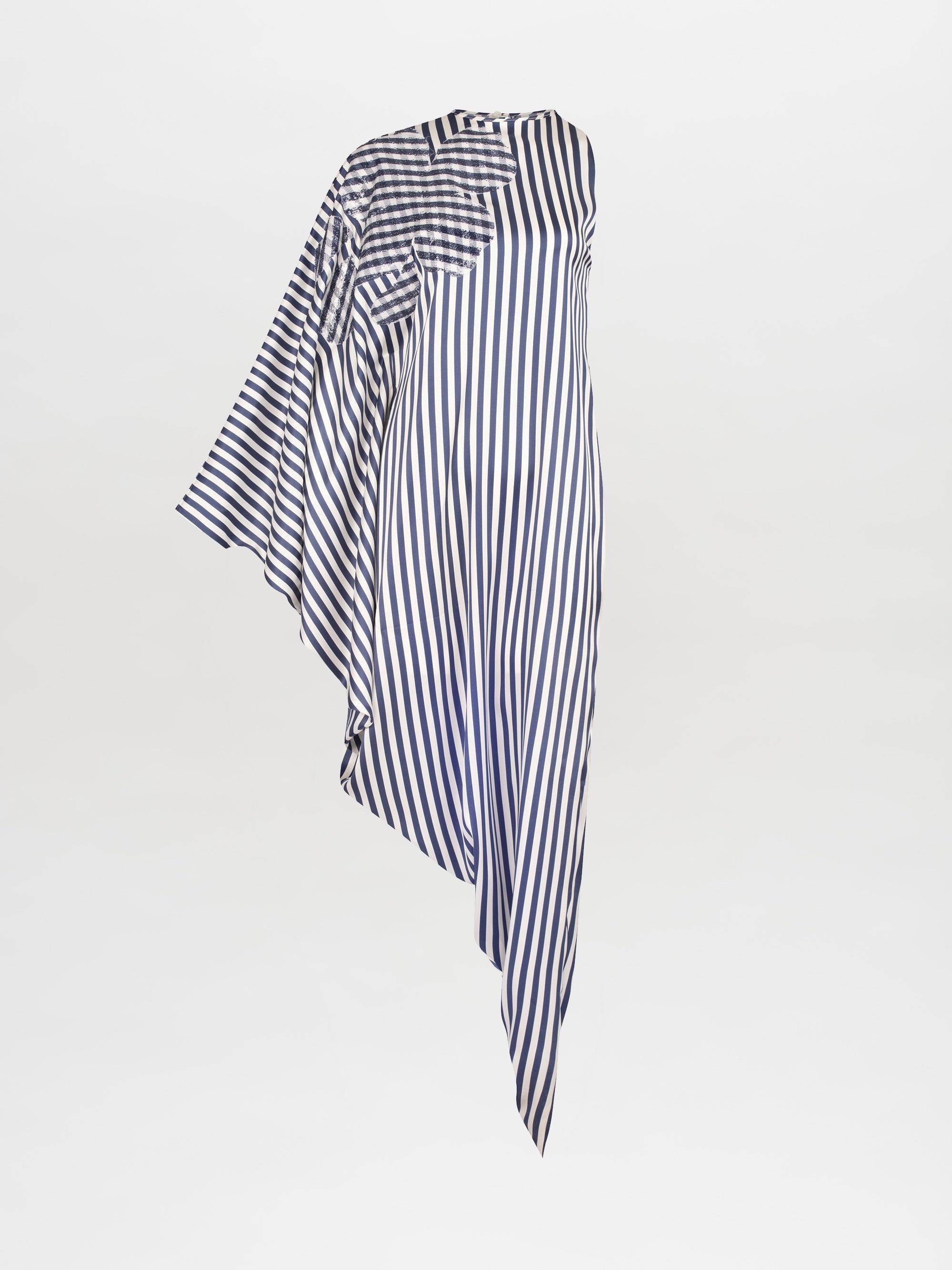 Person wearing the Golda Dress in White and Blue Stripes, an asymmetrical design with draped fabric, paired with white strappy sandals featuring embellishments, standing against a plain white background. Pre-order now to ensure it ships by February 15th, 2025.