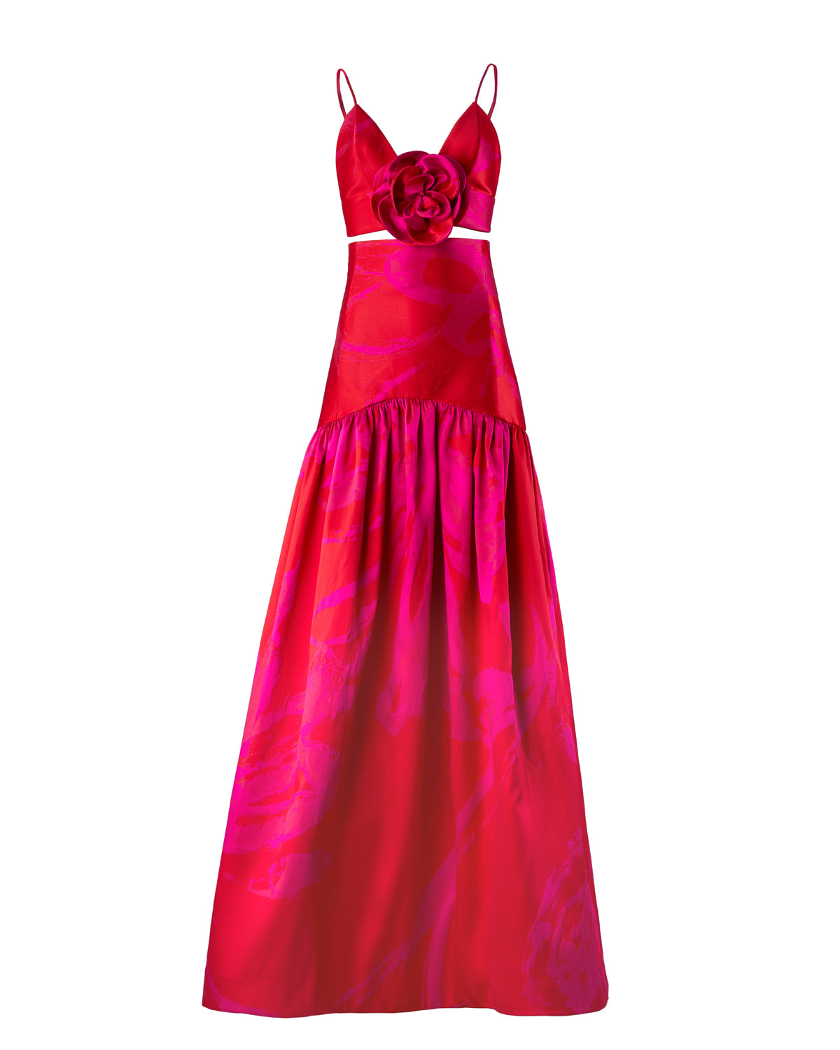 A person is standing wearing the Helen Set Dress Rouge Fuchsia Flower, a red, sleeveless gown featuring a floral detail on the bodice and a long skirt. The background is plain white. This stunning piece will be available for pre-order soon, with an expected ship-by date in early 2025.