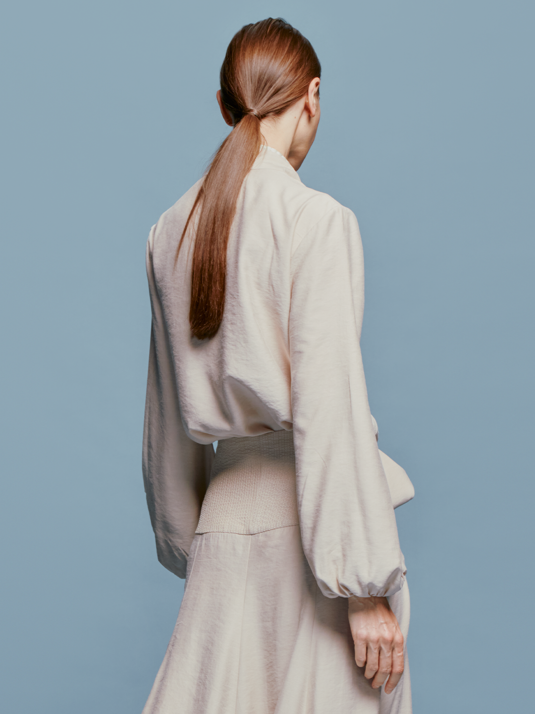 Person in a Honey Blouse Cream with a bow, wearing a long necklace, stands against a plain blue background, marking the date as either August 19th, 2024, or September 2nd.