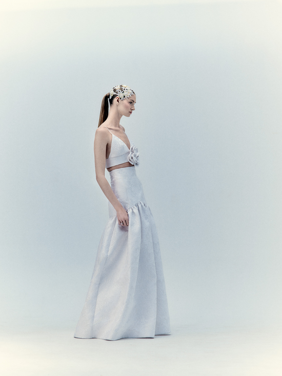 A woman in a Helen Set Dress Pearl with a floral headpiece posing against a light gray background.