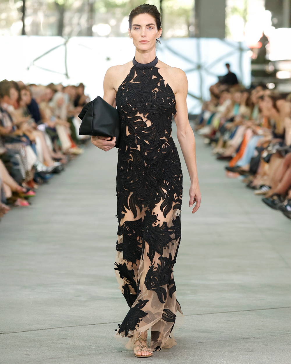 Model walking on a fashion show runway wearing a black and beige floral dress.