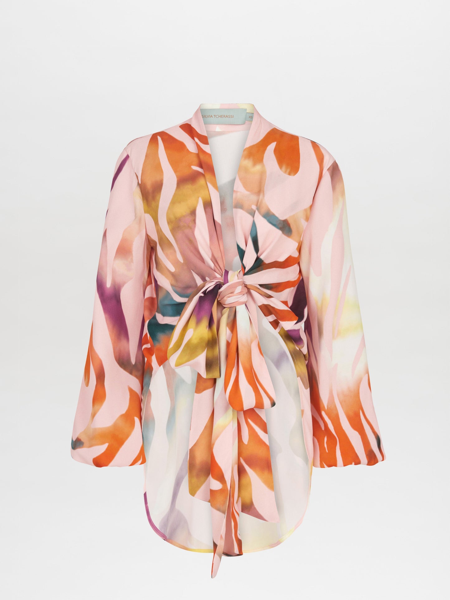 The Honey Blouse Blush Prismatic is a long-sleeve top with a vibrant abstract zebra print in pink, orange, yellow, and white. It features a front tie knot design and a flowy silhouette.