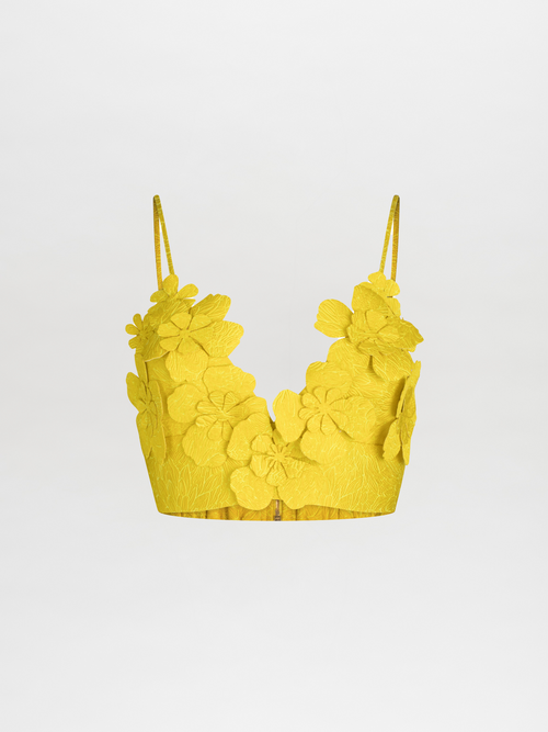 The Ibbie Top Limoncello is a yellow cropped top with floral appliqué and thin straps, expertly crafted from jacquard textured fabric, set against a plain background.