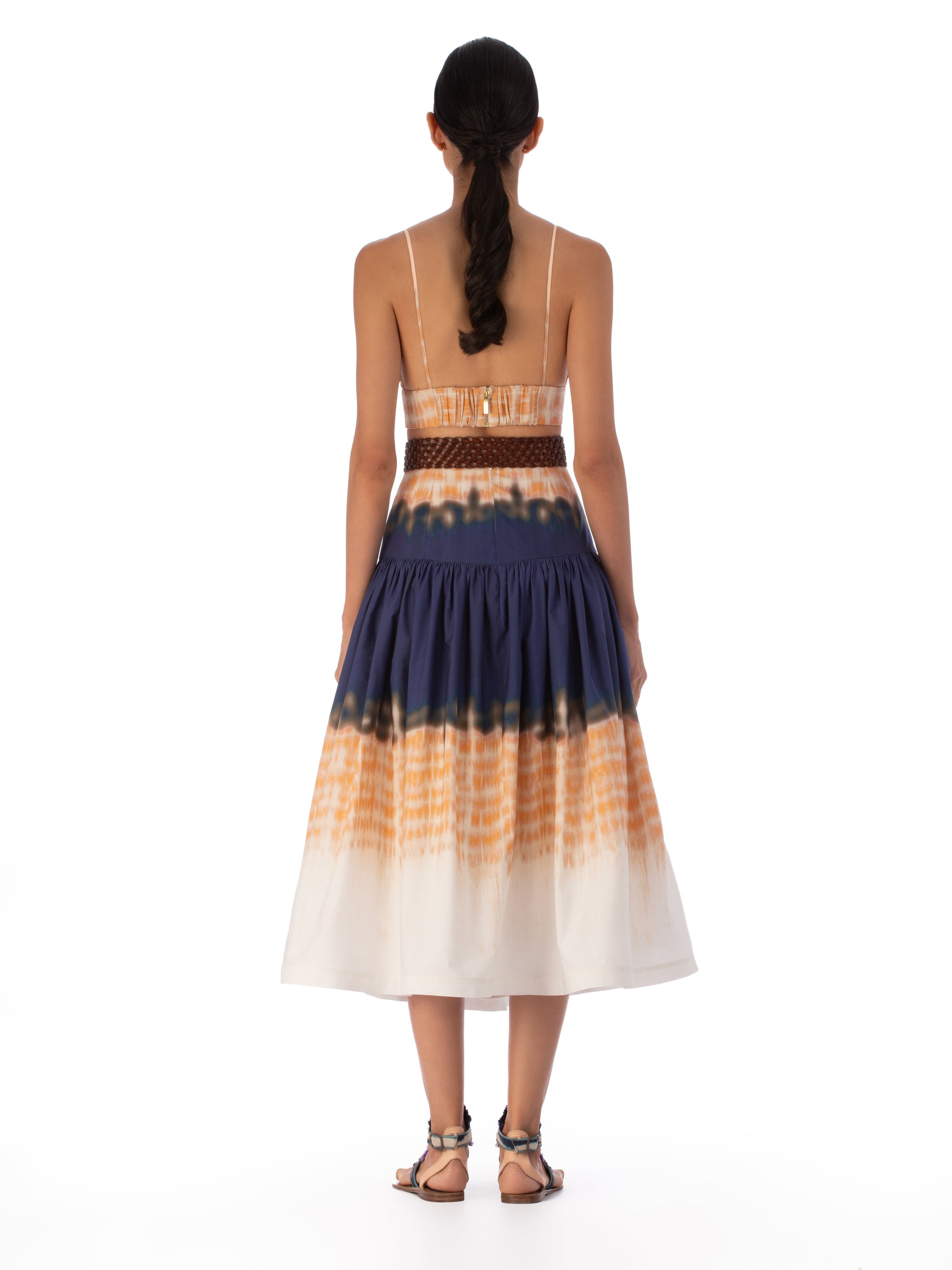The Halsey Skirt Mediterranean Coral Blue is a high-waisted, flared midi skirt crafted from 100% cotton. It features an abstract multicolor print in navy, orange, and white with a vibrant tie-dye pattern that adds a playful touch to any ensemble.