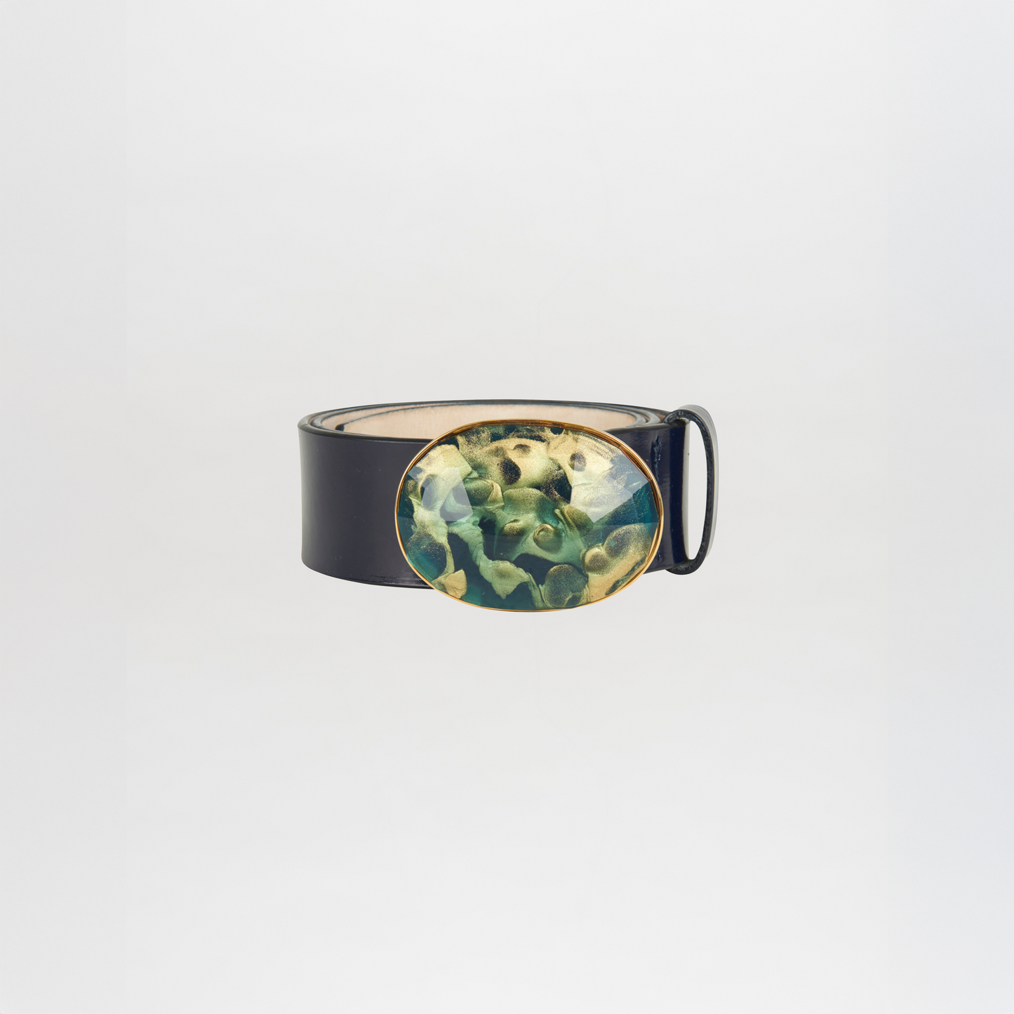 The Irene Belt Navy is a black Italian leather belt with a large oval buckle in green and gold abstract resin, shown on a plain white background. Ideal for elevating your Fall 2023 wardrobe.
