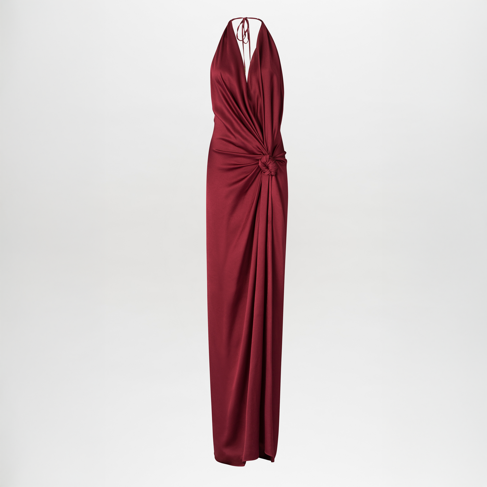 The Jazmin Dress is a deep red maxi dress featuring a twisted knot detail at the waist, draping elegantly to the floor with a flowing silhouette against a plain white background.