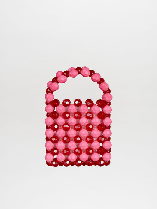 The Jasy Handbag Vermillon-Pink is a small, rectangular handbag adorned with red and pink beads, featuring a round bead handle that creates a textured effect against its plain background.