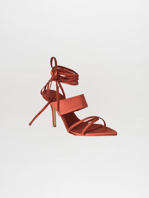 The Jimena Heels Bronze, crafted from luxurious Italian calf leather in a rich rust hue, boast elegant ankle ties and a pointed toe. These exquisite shoes are part of the Silvia Tcherassi collection and are beautifully showcased on a light background.