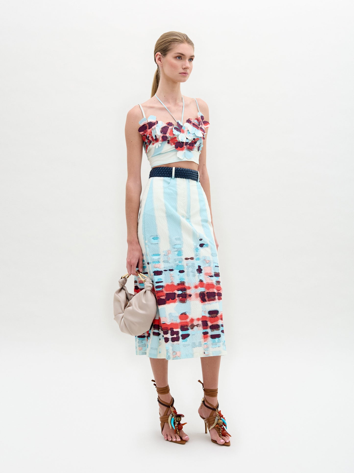 A person wears the Layan Skirt as a sleeveless patterned dress, paired with a beige bag and tassel-adorned strappy sandals.
