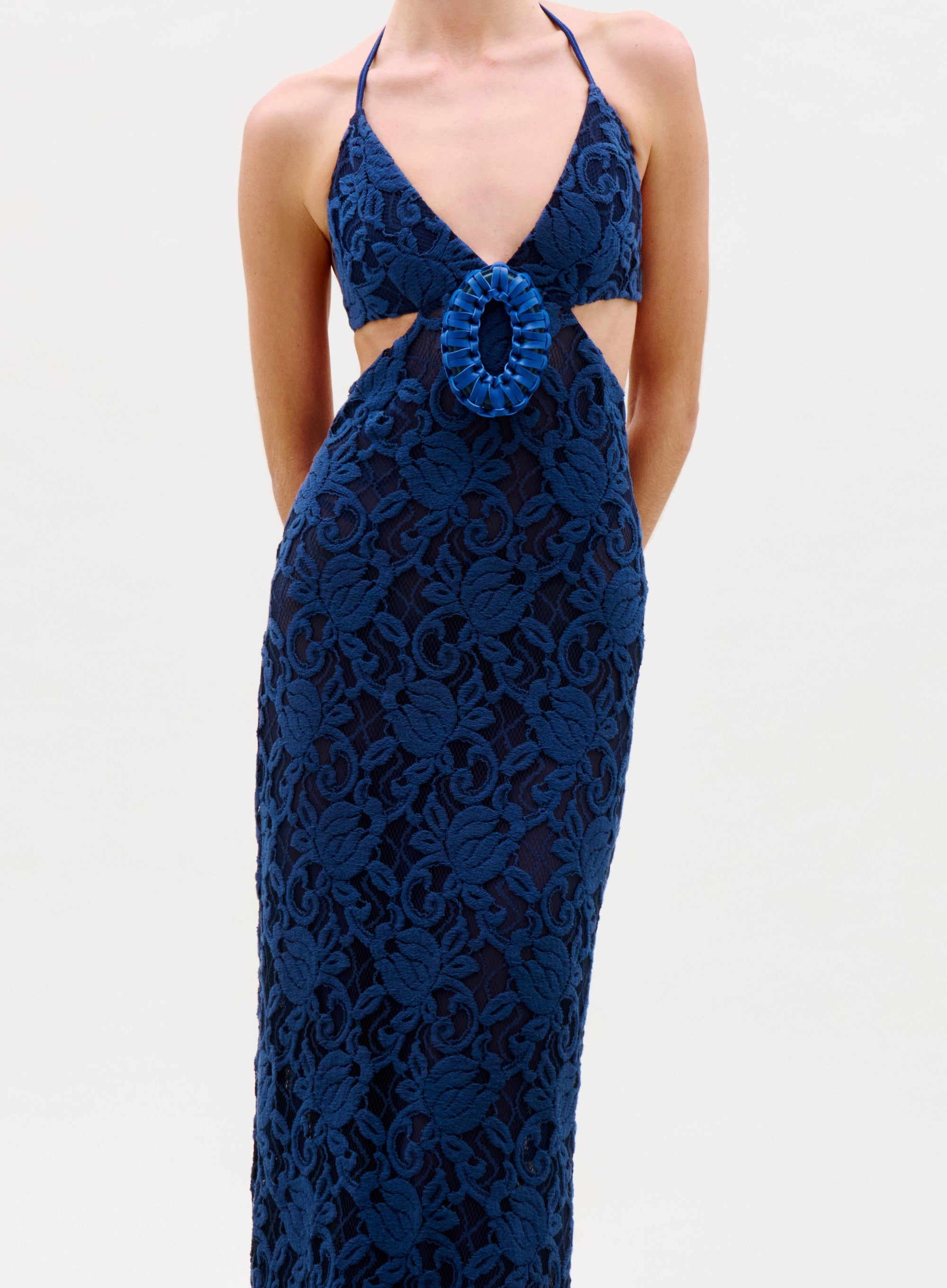 Someone is wearing the Karen Dress, a sleeveless navy blue lace dress with a halter neckline and central cutout, standing against a plain light background.