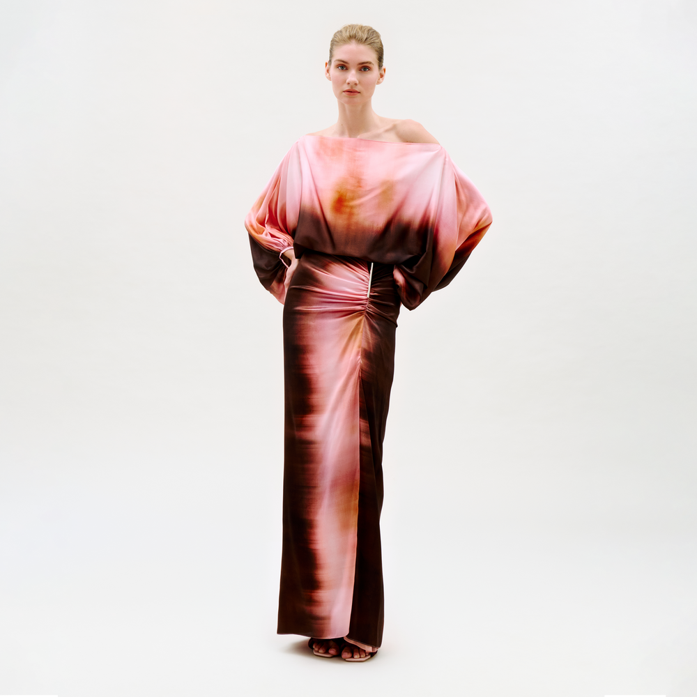 A woman stands confidently against a plain background wearing the Keiry Skirt, featuring an abstract pink, orange, and brown pattern with a flowing silhouette. She looks directly at the camera.