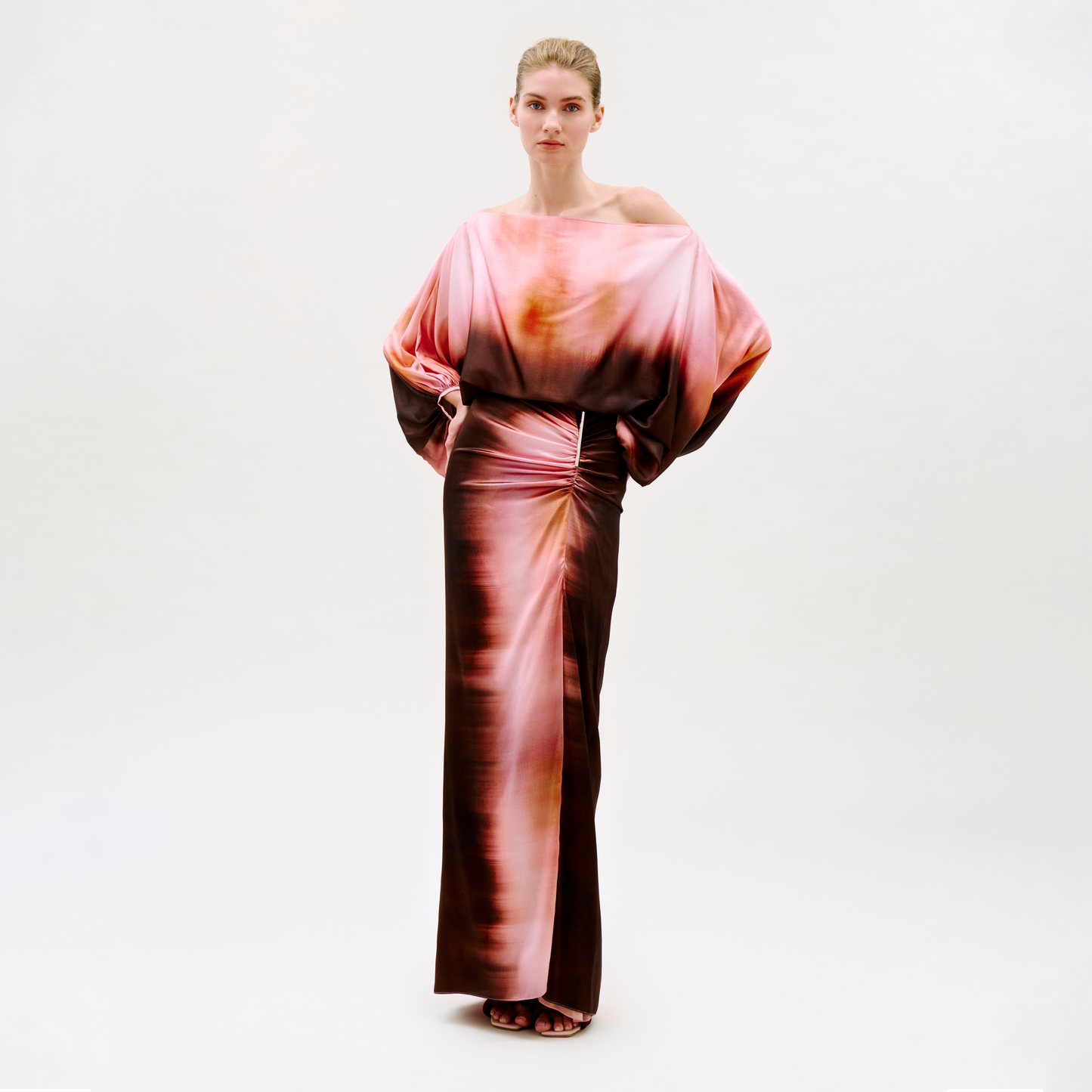 A woman stands confidently against a plain background wearing the Keiry Skirt, featuring an abstract pink, orange, and brown pattern with a flowing silhouette. She looks directly at the camera.