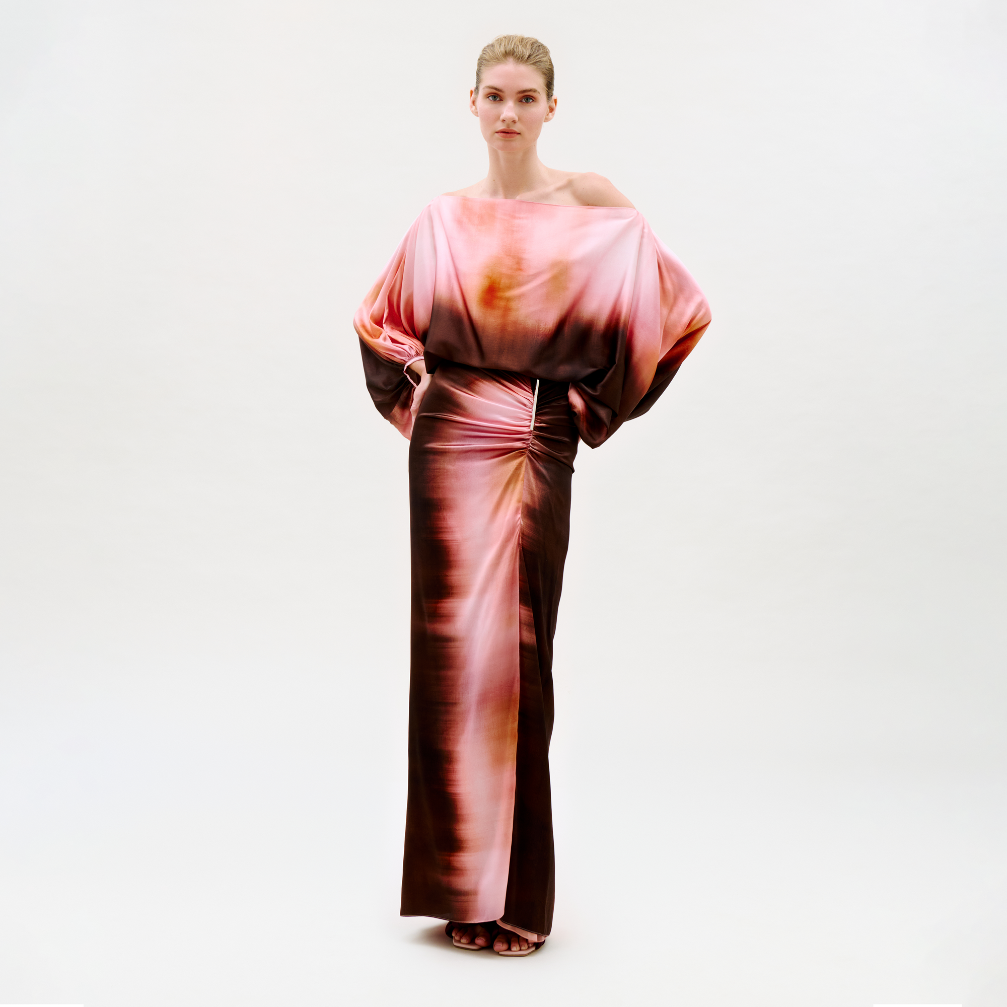 A woman stands confidently against a plain background wearing the Keiry Skirt, featuring an abstract pink, orange, and brown pattern with a flowing silhouette. She looks directly at the camera.