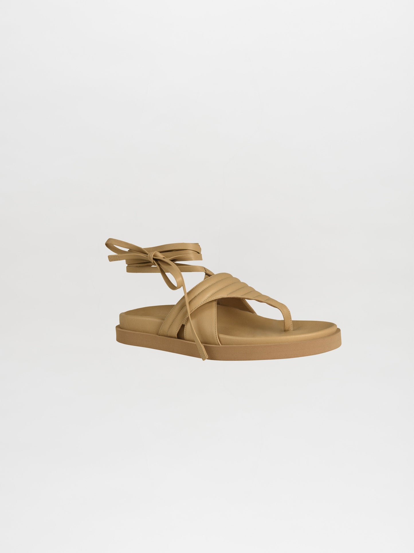 The Kristina Sandals Beige, made from luxurious Italian calf leather, showcase a flat sole, quilted toe-thong design, and elegant ankle laces against a simple white background—a versatile staple for any wardrobe.