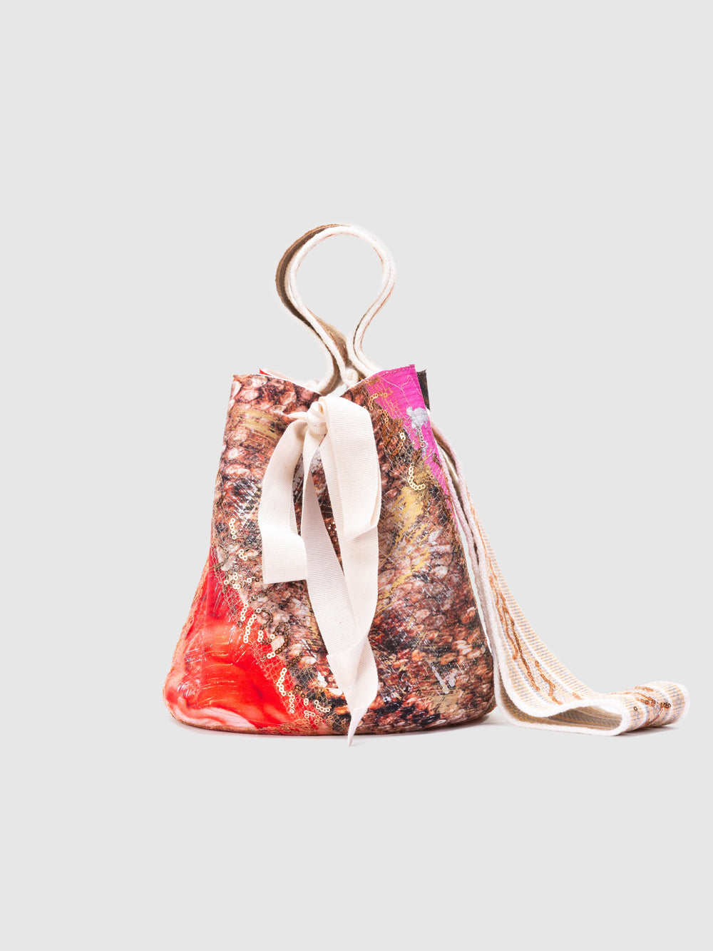 The Mochila Laaput Big is a small handmade bucket bag featuring a multicolored abstract pattern, white ribbon drawstrings, and a long shoulder strap, beautifully displayed against a plain light background.