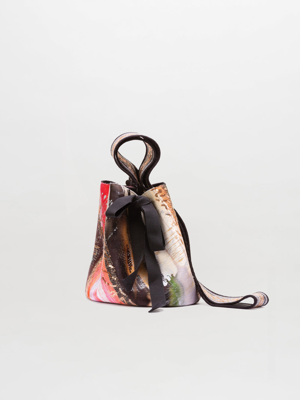 The Mochila Laaput Small is a compact bucket bag featuring an abstract multicolor print, a knotted top handle, black ribbon details, and a hand-woven strap inspired by traditional Wayuu mochila handbags, shown on a plain light background.