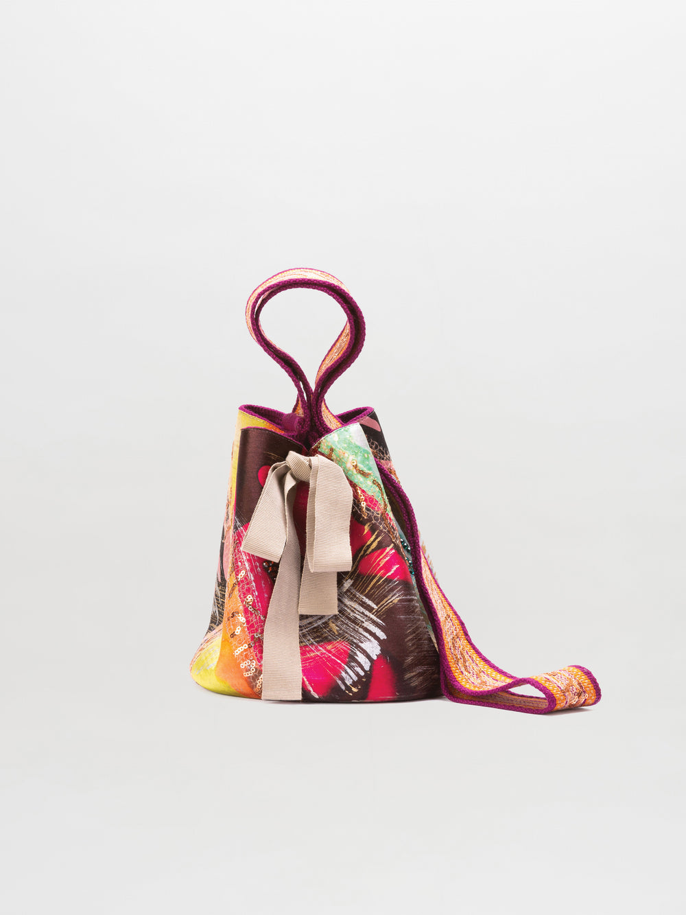 The Mochila Laaput Small is a colorful hand-woven bucket bag featuring a butterfly print, beige ribbon tie, and circular handle, shown against a plain white background.