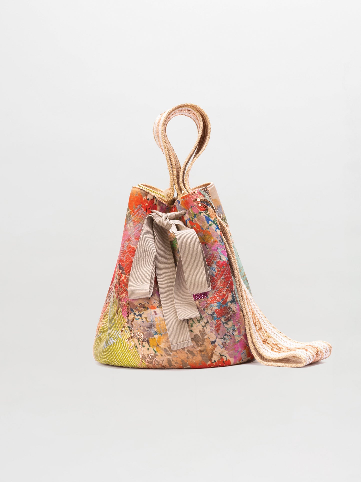 The Mochila Laaput Beige is a colorful, patterned Wayuu handbag featuring beige fabric handles and a matching beige bow, displayed against a plain light background.