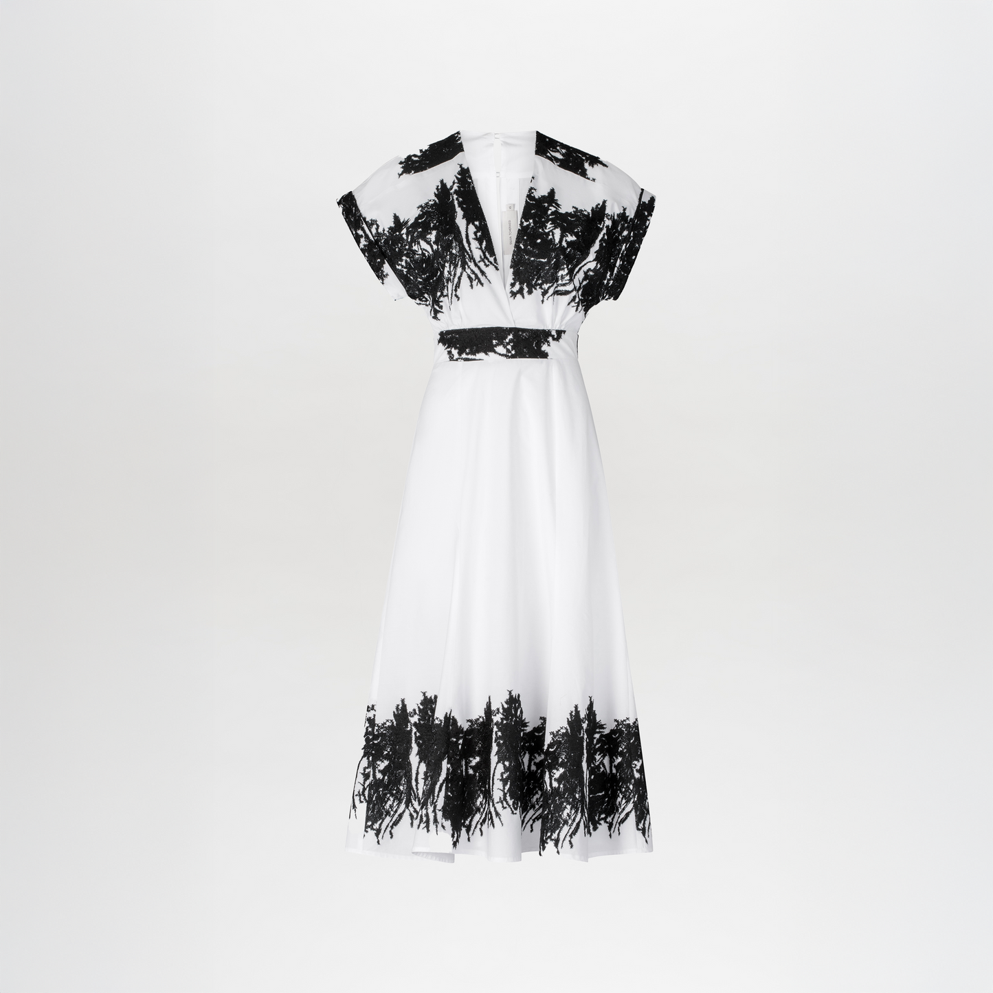 The Laila Dress features a white canvas with contrasting patterns, embroidered black floral details on the sleeves, waist, and hem, and is complemented by a V-neck and short sleeves against a plain backdrop.