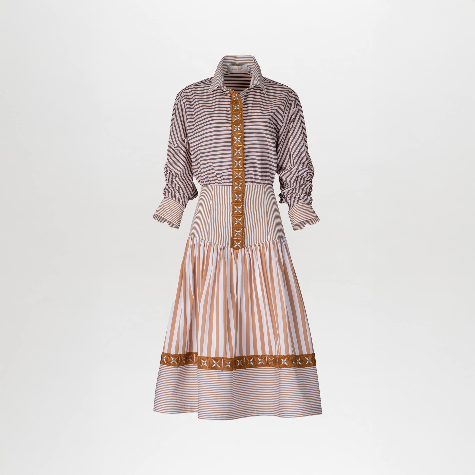 A woman stands against a blue background, wearing the Lamar Dress in Multi Brown Stripes, accentuated with a belt and boots, evoking the spirit of an August 19th summer day.