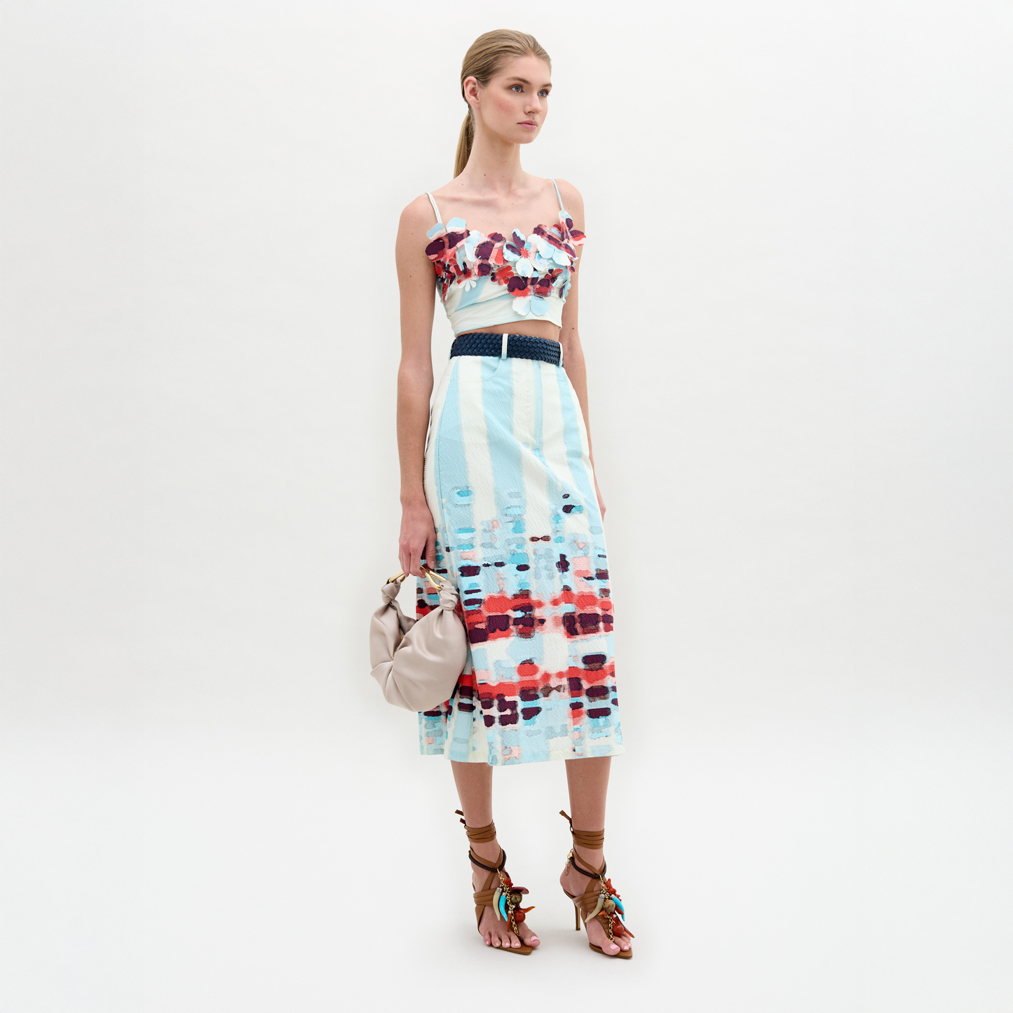 A person wears the Layan Skirt as a sleeveless patterned dress, paired with a beige bag and tassel-adorned strappy sandals.