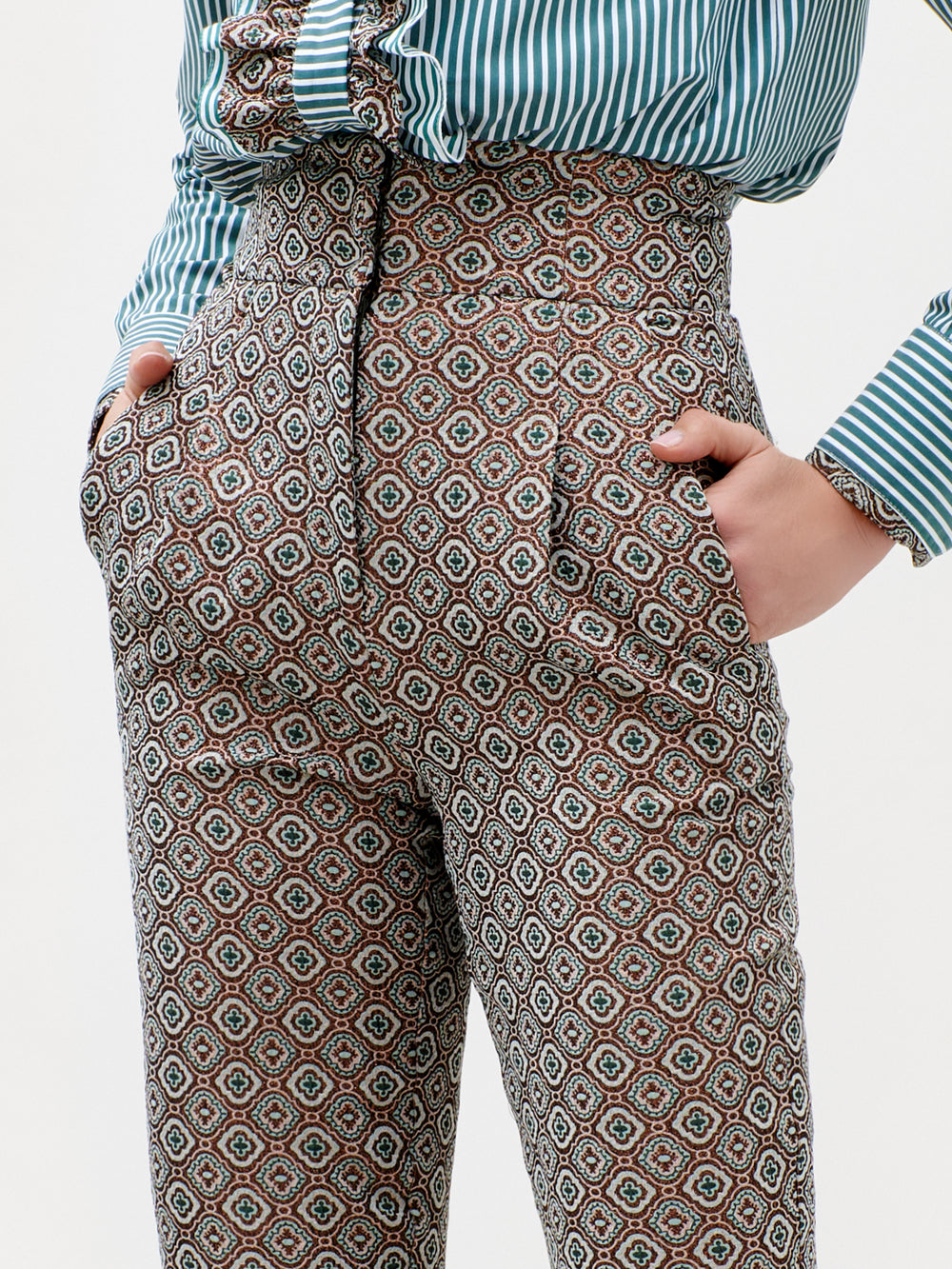 Person wearing the Luca Pant—high-waisted and patterned, crafted from luxurious Italian fabric—with hands in pockets and a green-and-white striped shirt. The image centers on the pants and part of the shirt; head and lower legs are not visible. Made in Colombia.