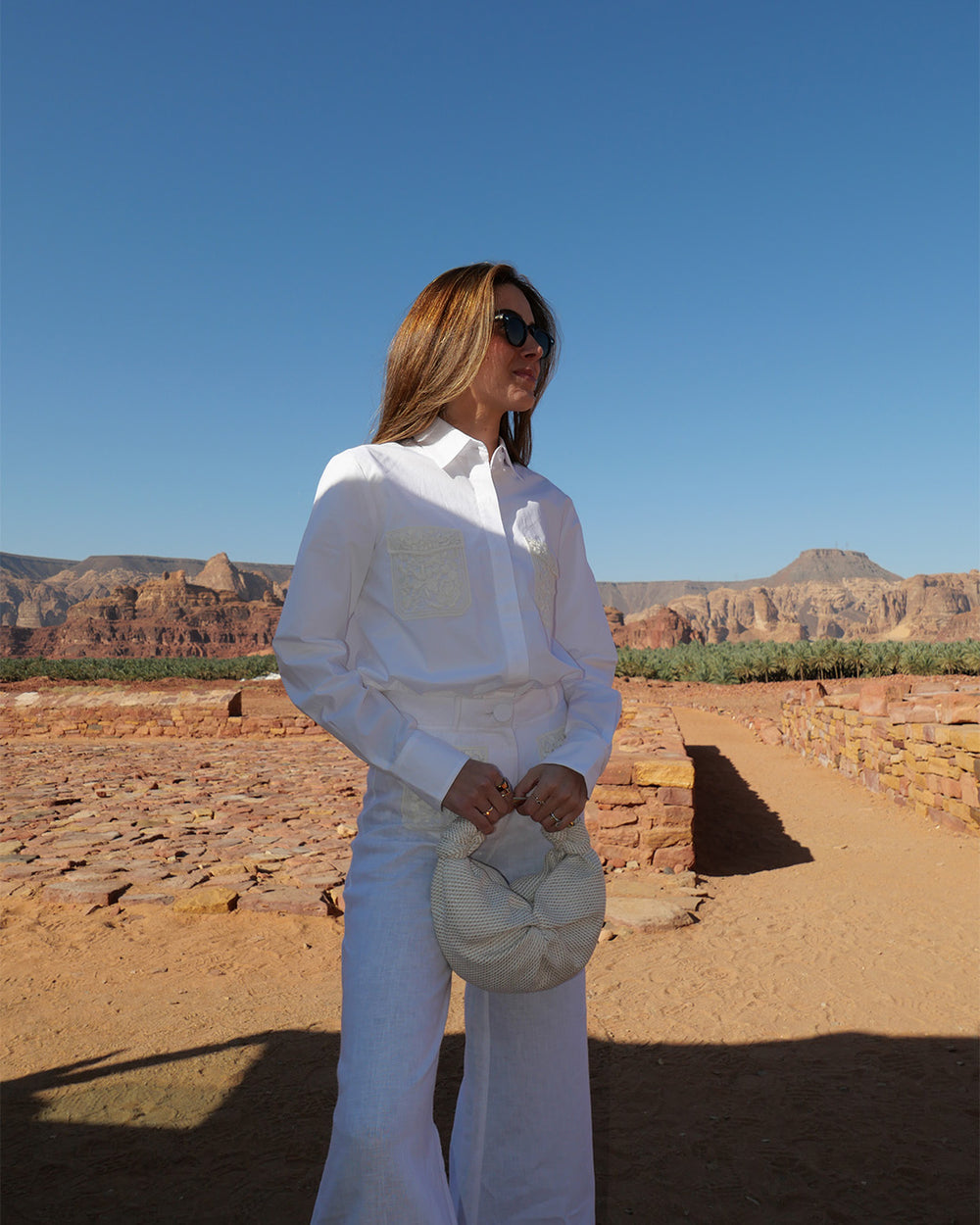 Woman in white outfit standing in a desert landscape with clear blue sky