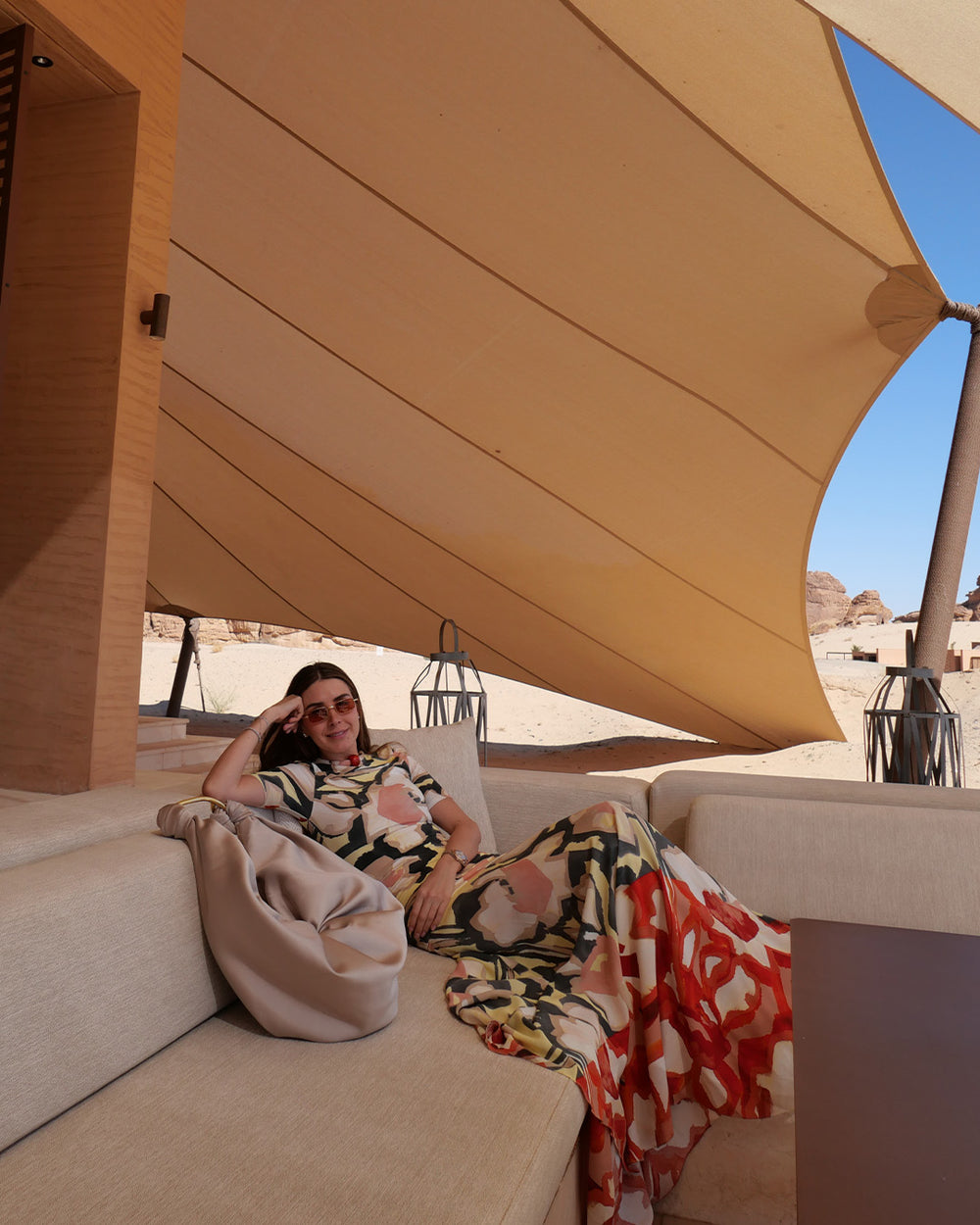 Woman sitting on a couch under a large beige shade structure with a desert landscape in the background.