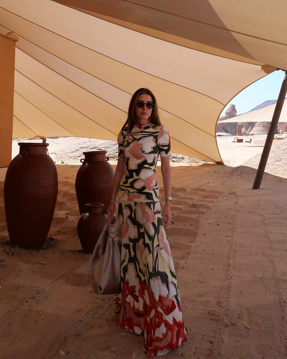 Woman in a colorful dress standing under a large beige tent with desert landscape in the background.