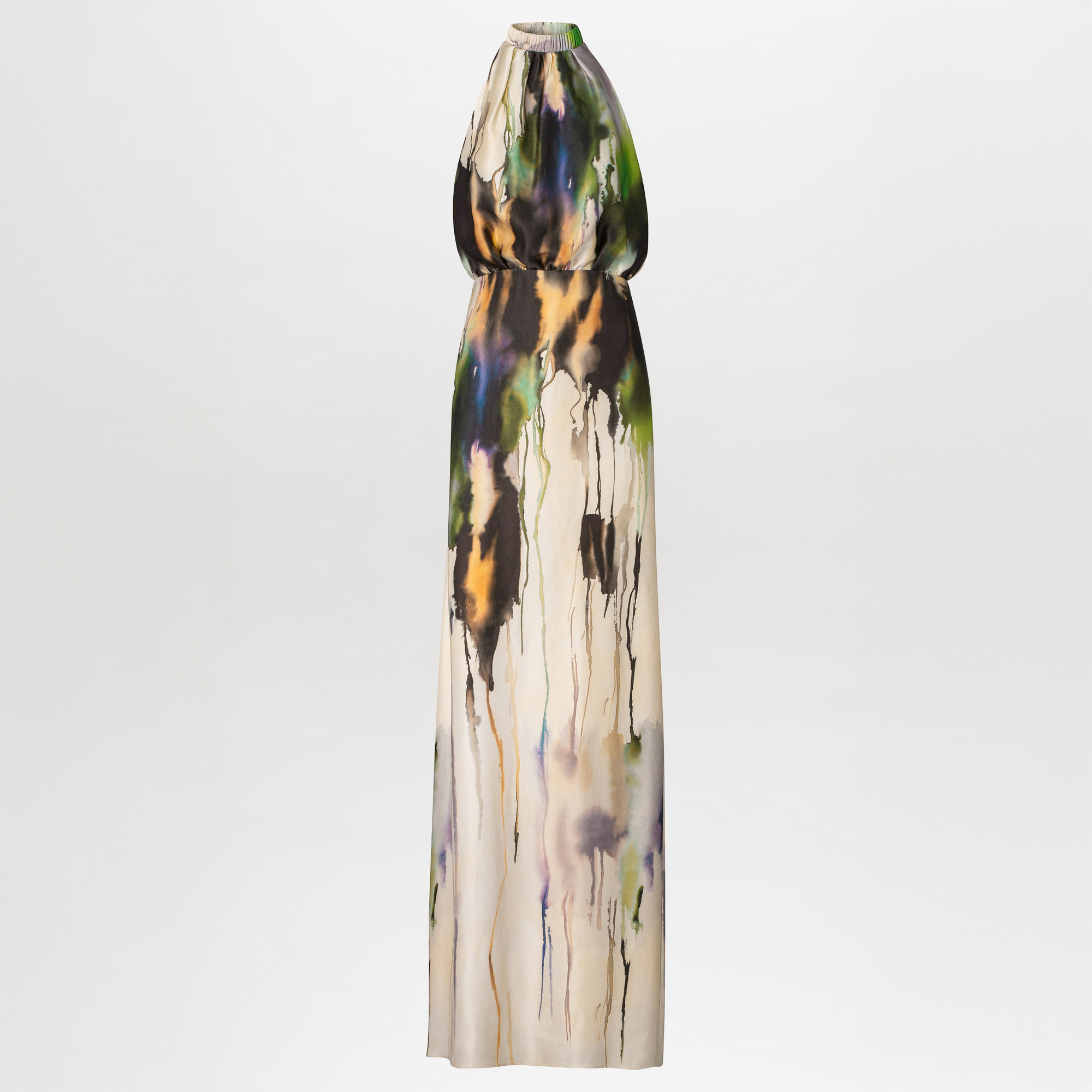 A woman in an elegant, long, Mabel Dress Olive Watercolor with an abstract design, available for pre-order, standing against a light blue background.