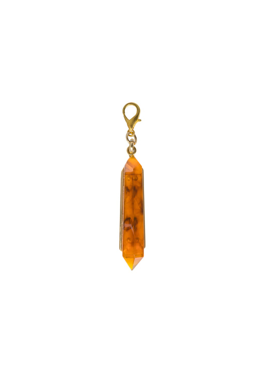 The Mariela Charm Amber features a golden clasp attached to an elongated, faceted orange gemstone, and is available for shipment starting September 2nd.