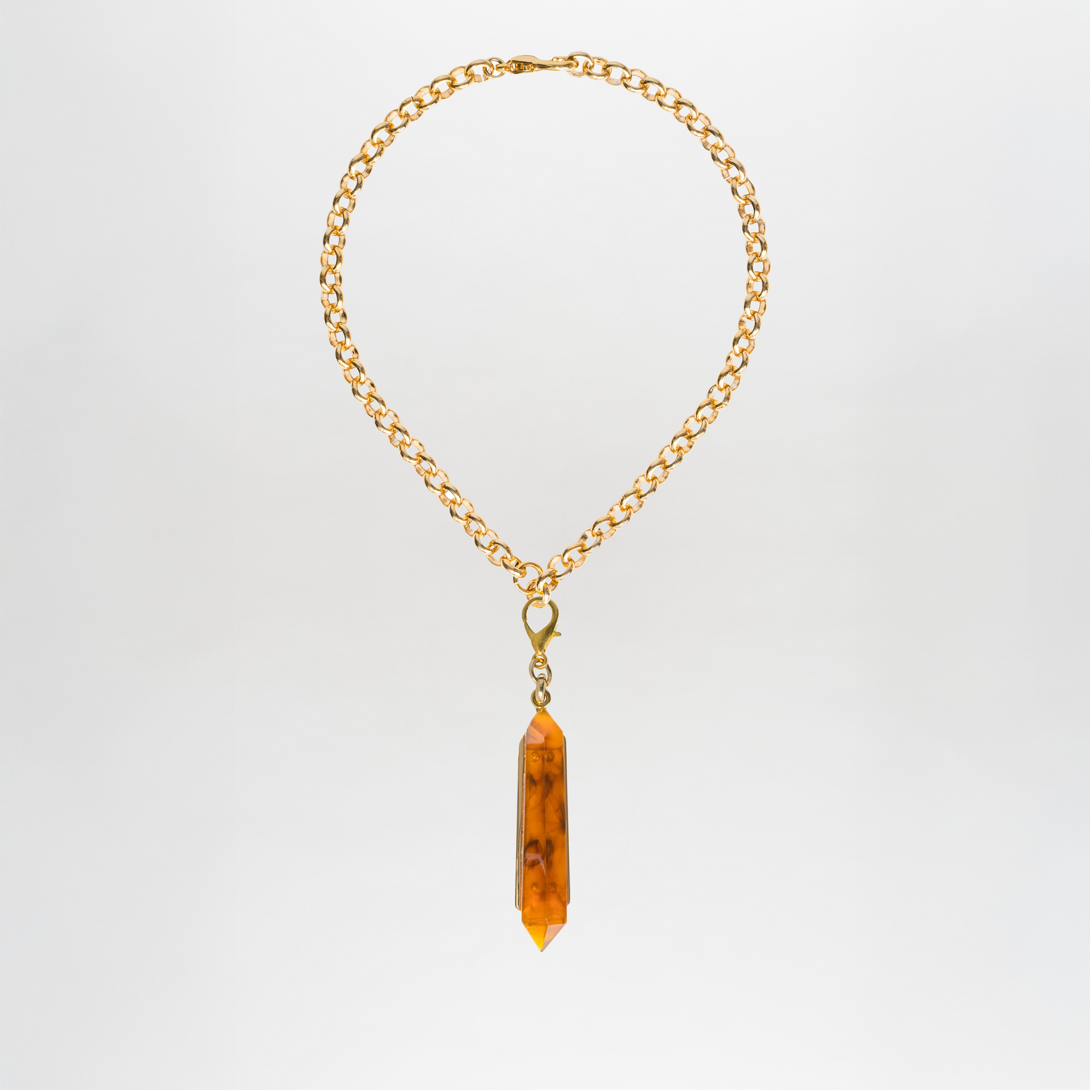 The Mariela Necklace is a gold chain adorned with a geometric crystal pendant, showcasing a striking elongated orange hue, beautifully displayed against a plain white background.