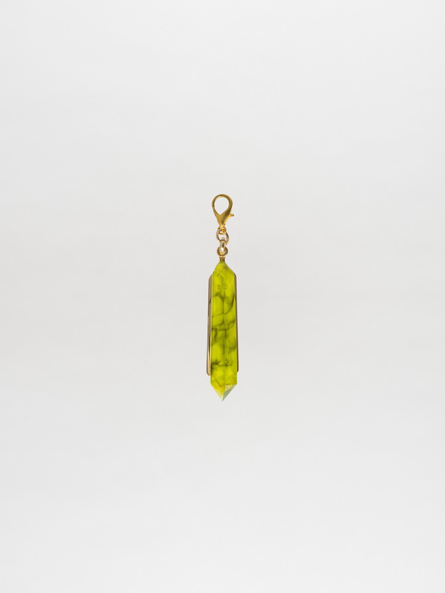 The Mariela Charm Green, by Tcherassi, is elegantly displayed against a plain white background, showcasing a green gemstone pendant with a gold clasp and an enchanting crystal charm.