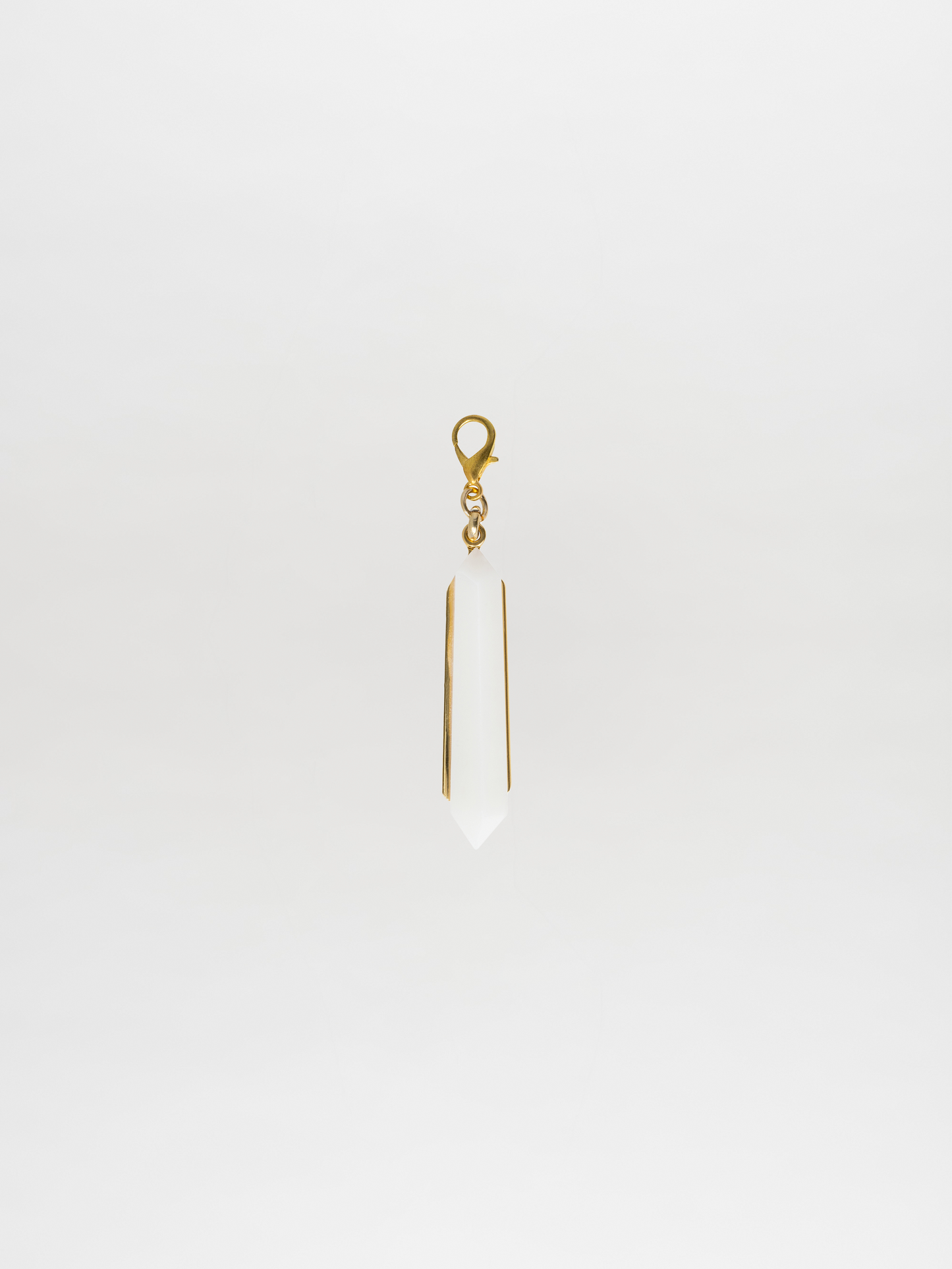 The Mariela Charm Pearl, a gold-tone and white crystal pendant crafted in a pointed shape, elegantly hangs against a plain white background, showcasing the signature Tcherassi design.