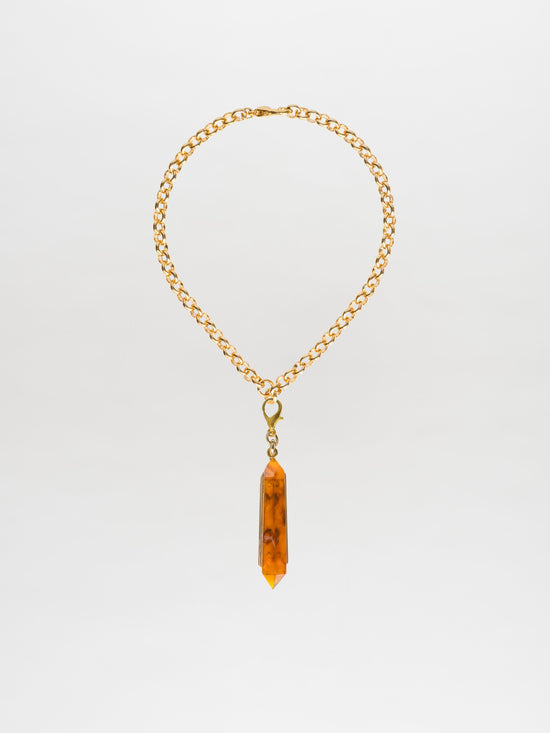 The Mariela Necklace Amber features a chic choker style, with a gold-plated brass chain adorned by a geometric crystal pendant in an amber hue.