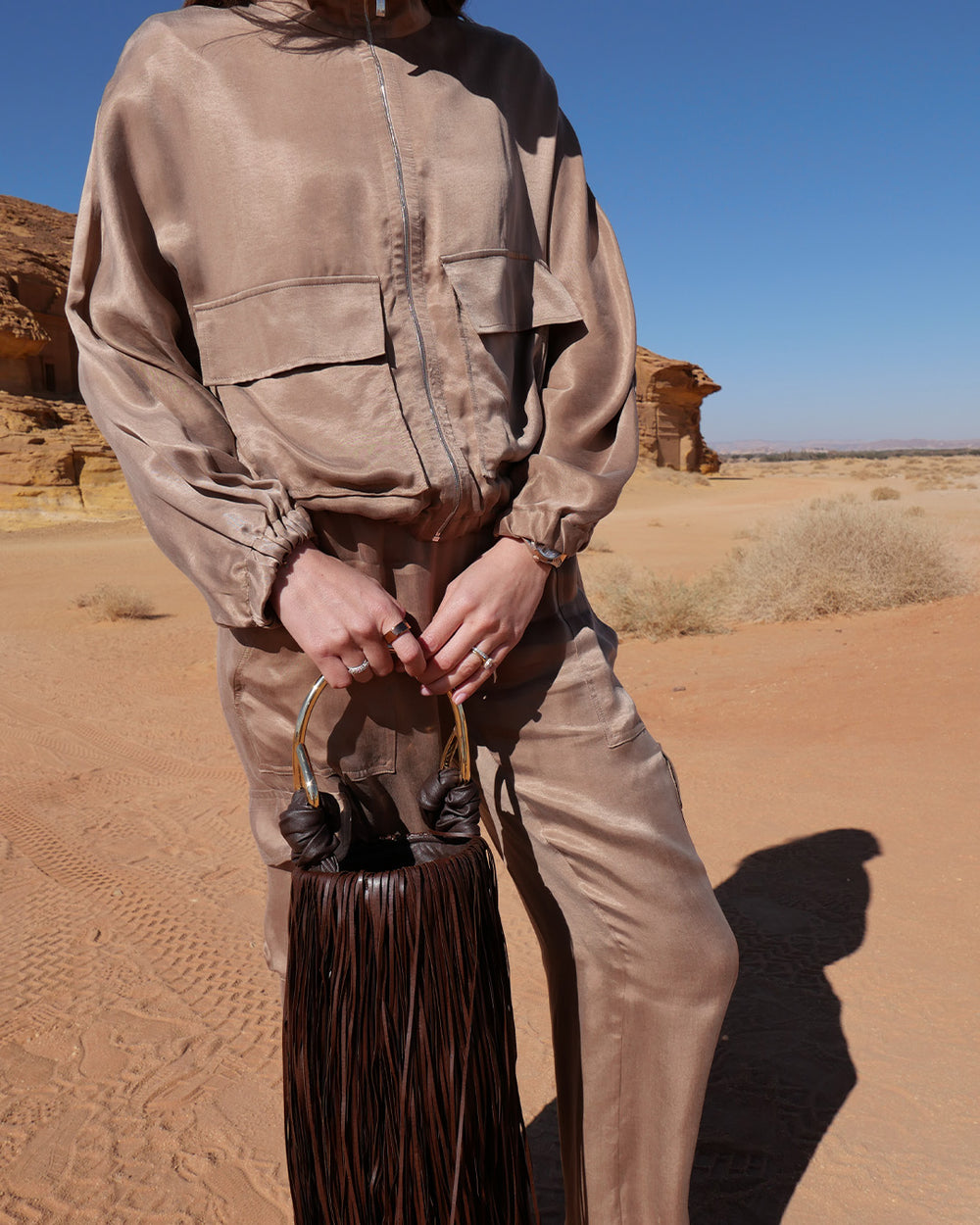 Person in beige jacket holding a brown bag in a desert landscape