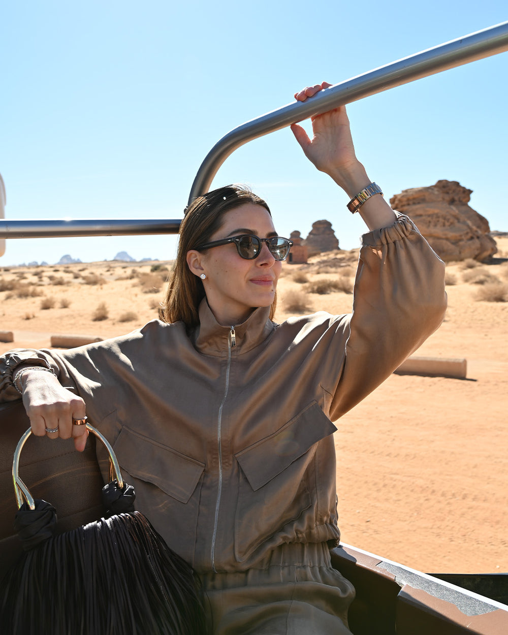 Woman in a beige jacket sitting in an open-top vehicle in a desert landscape.