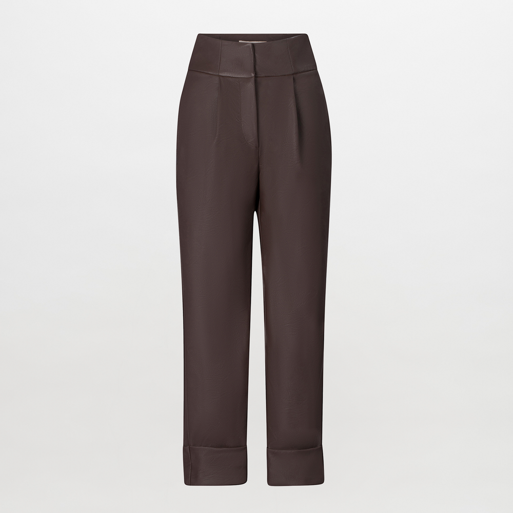 A person is standing against a blue background, wearing a green and brown patterned shirt, dark pants referred to as the "Moad Pant Brown," and gray heeled boots. The shirt is partially tucked into the pants, creating a stylish look perfect for August 19th.